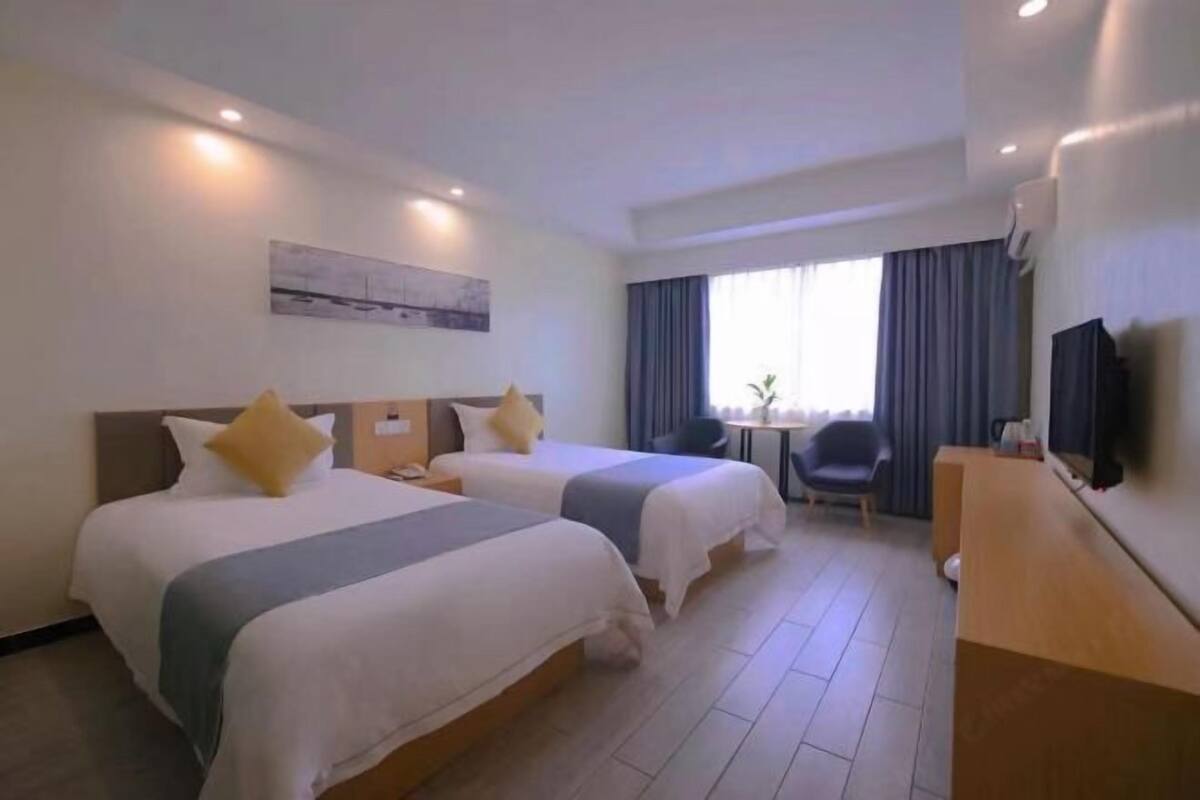 A hotel room with two beds, a desk, a chair, a television, and a window with curtains.