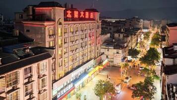 A multi-story hotel with a prominent sign, a street in front with trees and shops, and a clear view of the sky.