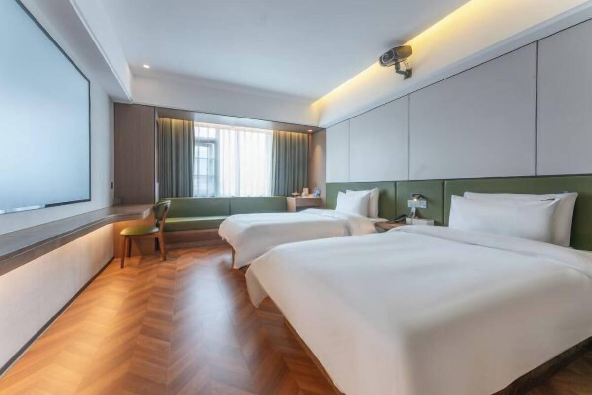 A hotel room with two beds, a chair, a nightstand, and a window with curtains.