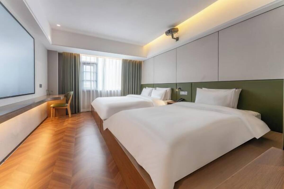 A hotel room with two beds, a large window, a chair, and a security camera.