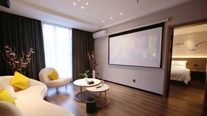 Une chambre d’hôtel moderne avec un canapé incurvé, une petite table ronde, un écran de projection et un lit.