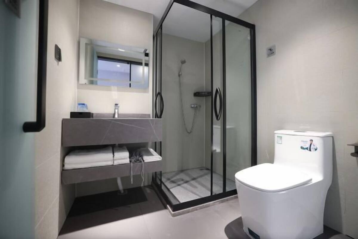 A modern bathroom with a glass-enclosed shower, a white toilet, and a vanity with a towel rack.