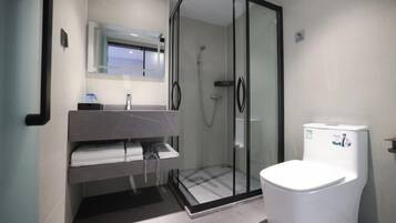 Un baño moderno con ducha de vidrio, inodoro blanco y tocador con perchero.