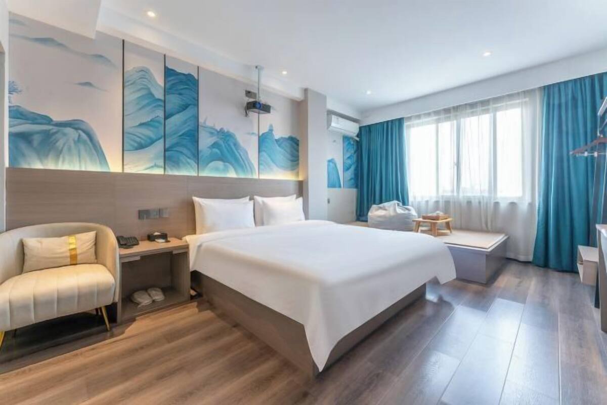 A modern hotel room with a large bed, a sofa, a desk, and a window with curtains.