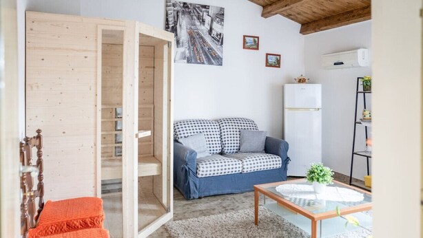A compact living space with a wooden wardrobe, a checkered sofa, a glass coffee table, and a white refrigerator.