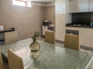 A compact kitchen with a microwave, stove, and cabinets. A dining table with chairs and a vase of flowers is in the foreground. - Casa Vacanze Francesca (Mondolfo)