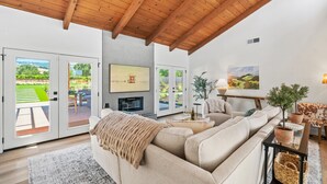 Un salon moderne avec un canapé beige, une cheminée et une grande fenêtre donnant sur un jardin.