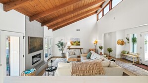 Un salon spacieux avec un haut plafond, une cheminée, un ensemble de canapés et un coin repas avec une banquette.
