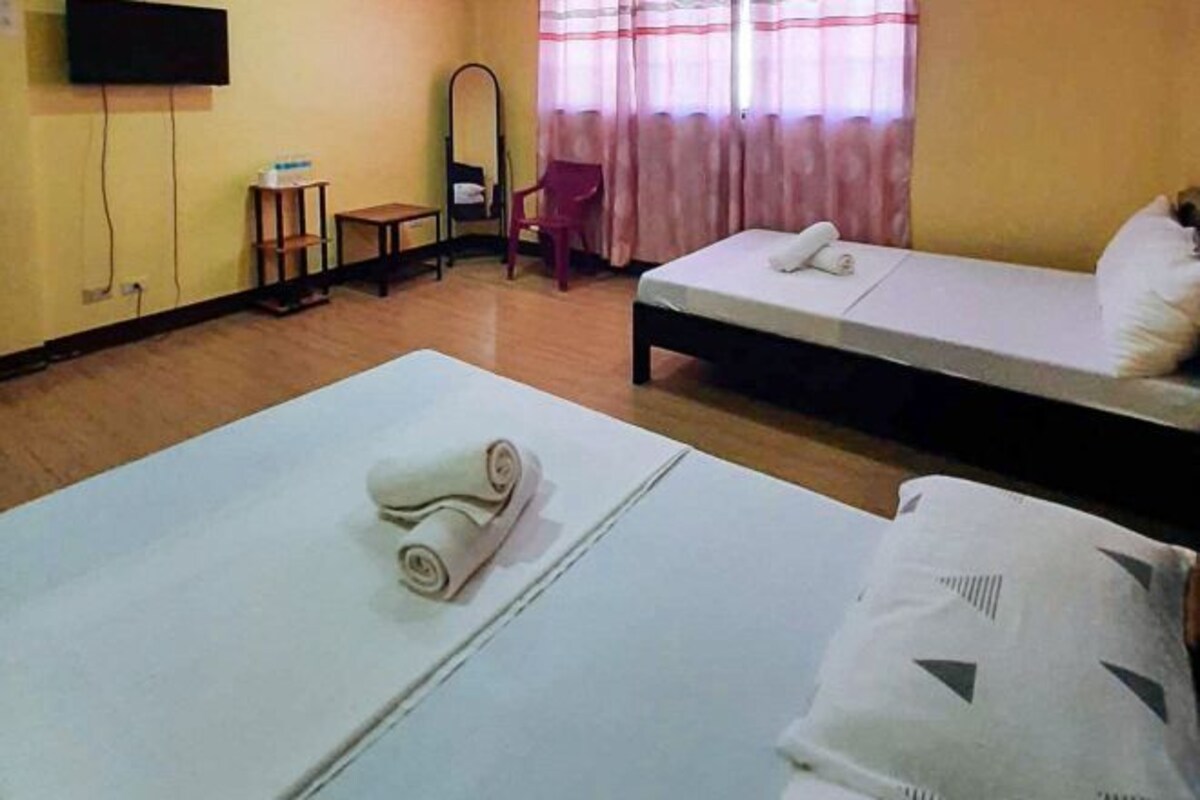 A hotel room with two beds, a TV mounted on the wall, a small table, and a chair.