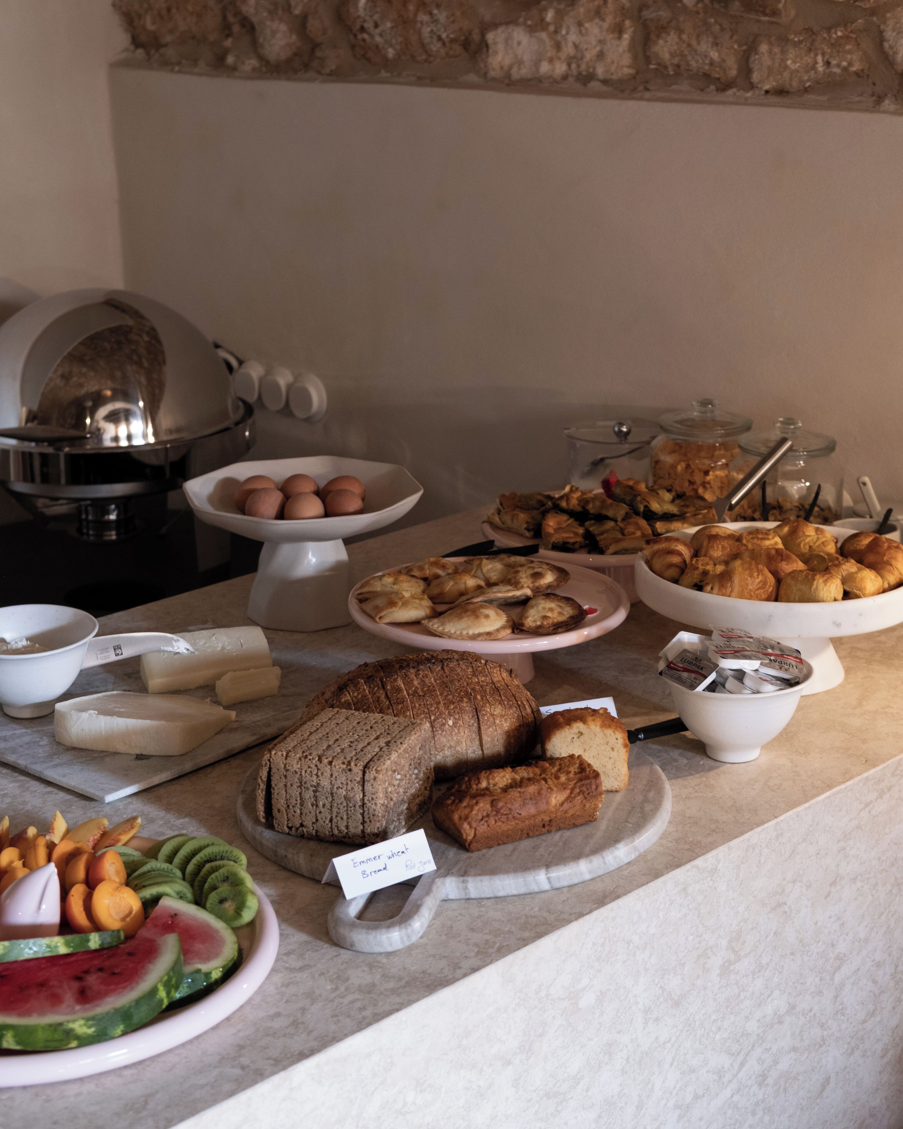 Un tavolo del buffet con diversi cibi, tra cui pane, pasticcini e frutta.