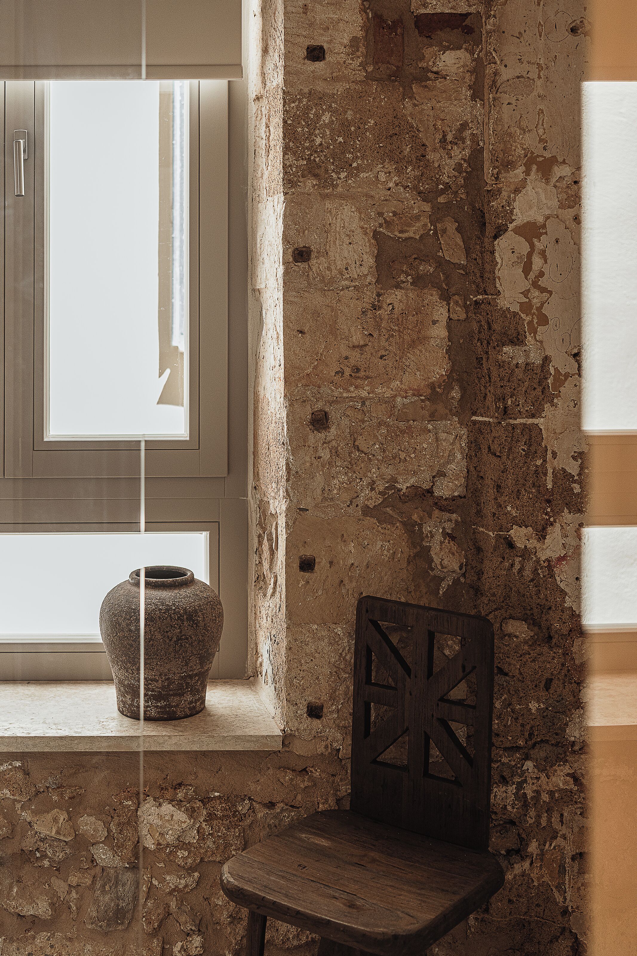 A rustic interior with exposed brick walls, a wooden chair, and a stone vase on a windowsill.