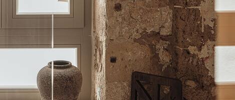 A rustic interior with exposed brick walls, a wooden chair, and a stone vase on a windowsill.