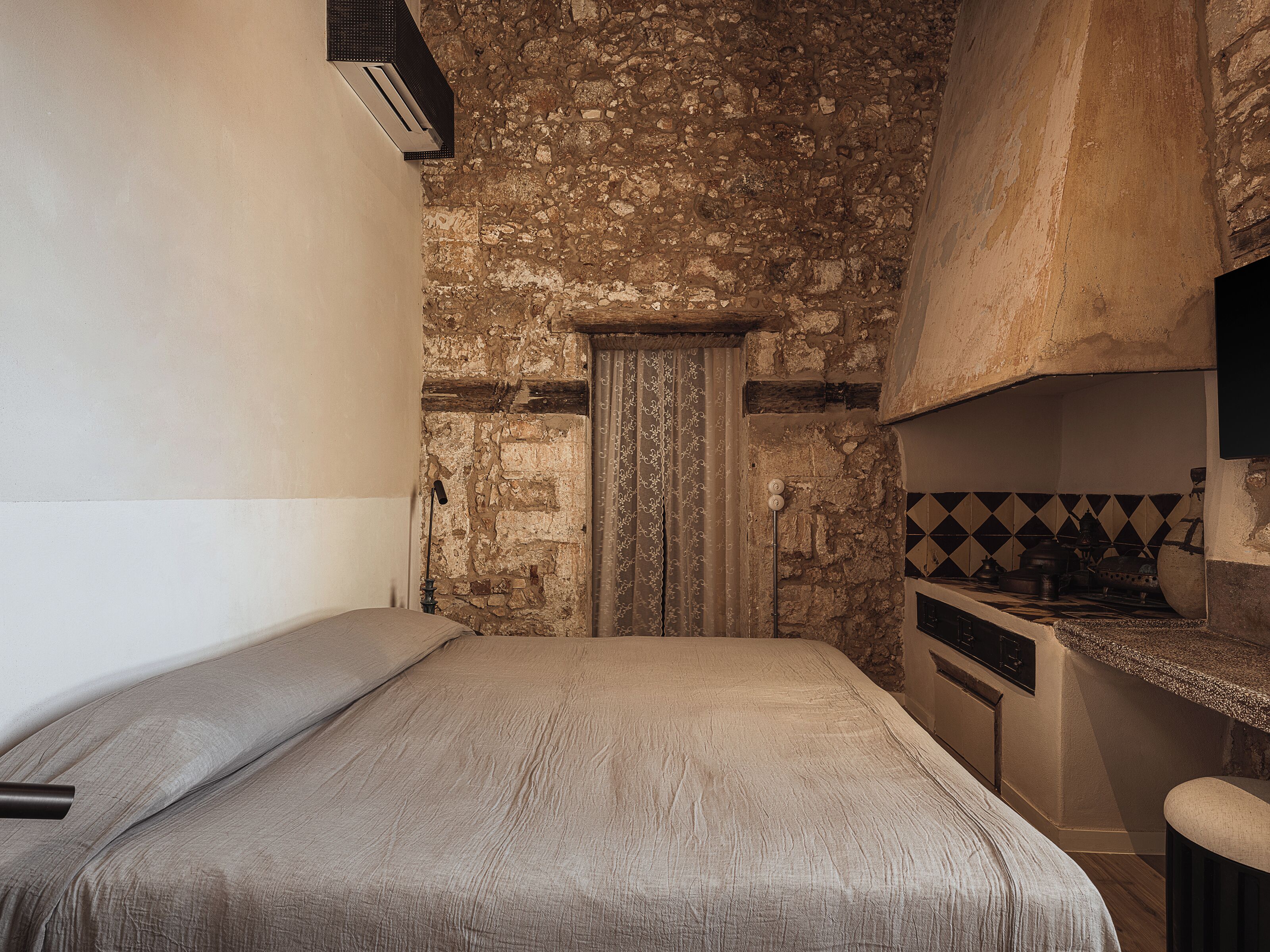 A compact bedroom with a bed, a small kitchenette, and a stone wall.