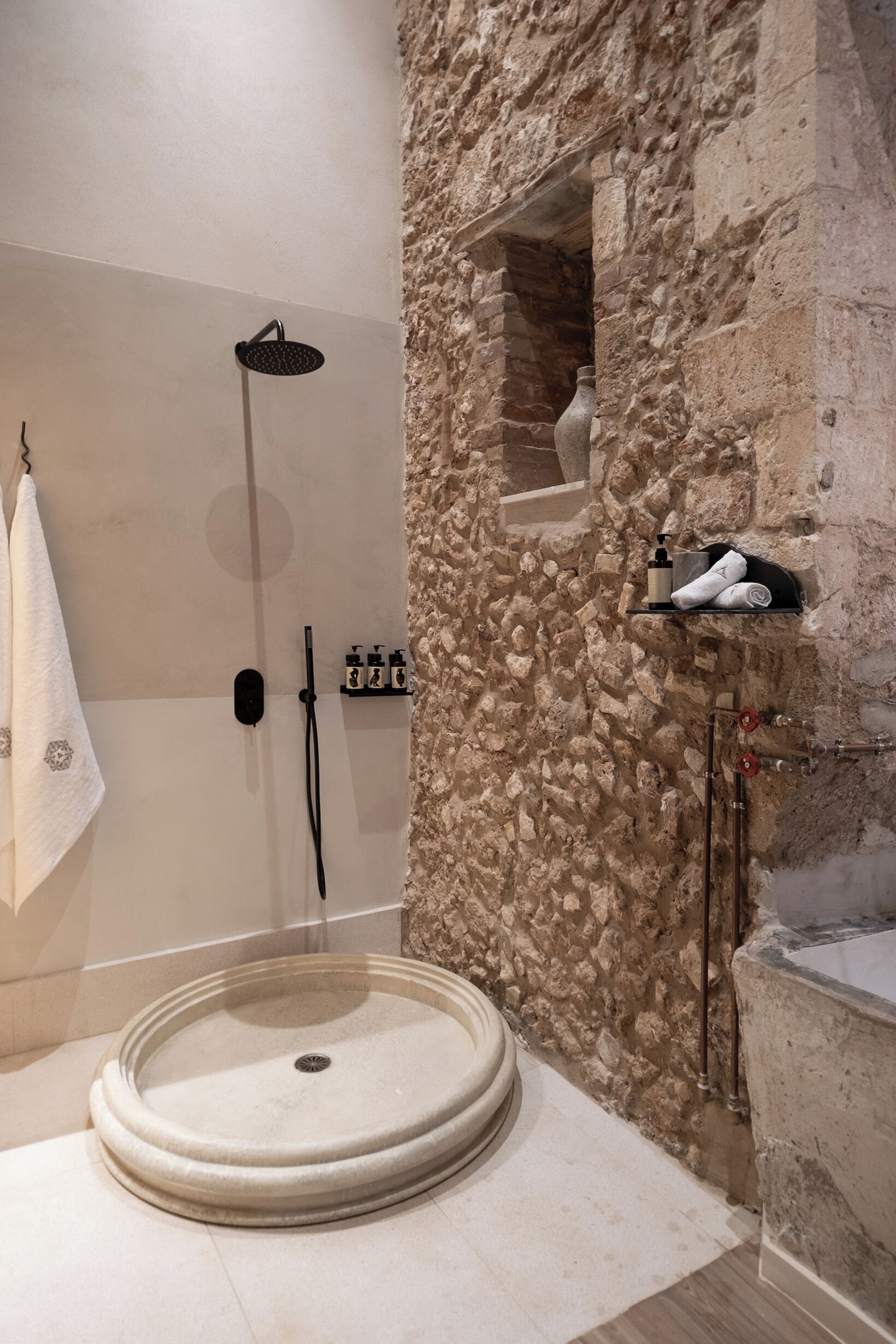 A bathroom with a stone wall, a round sink, and a shower.
