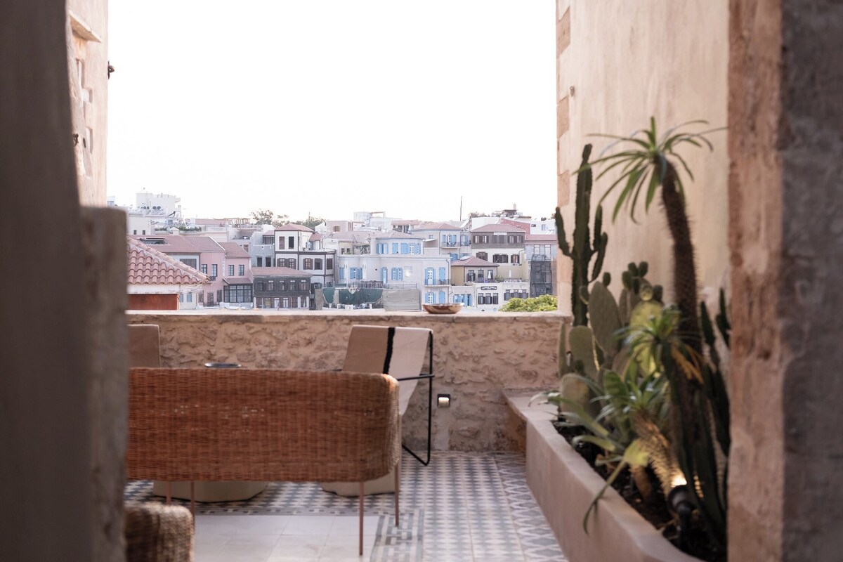 A balcony with wicker furniture, a view of buildings, and potted plants.