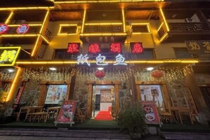 Ein Restaurant mit einer Steinfassade, leuchtenden Neonreklamen und einem roten Teppich vor dem Eingang.
