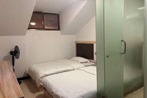 A small, single-room hotel room with two beds, a wooden desk, a fan, and a glass door. - Dajiuhu Juyuan Hotel (Shennongjia)