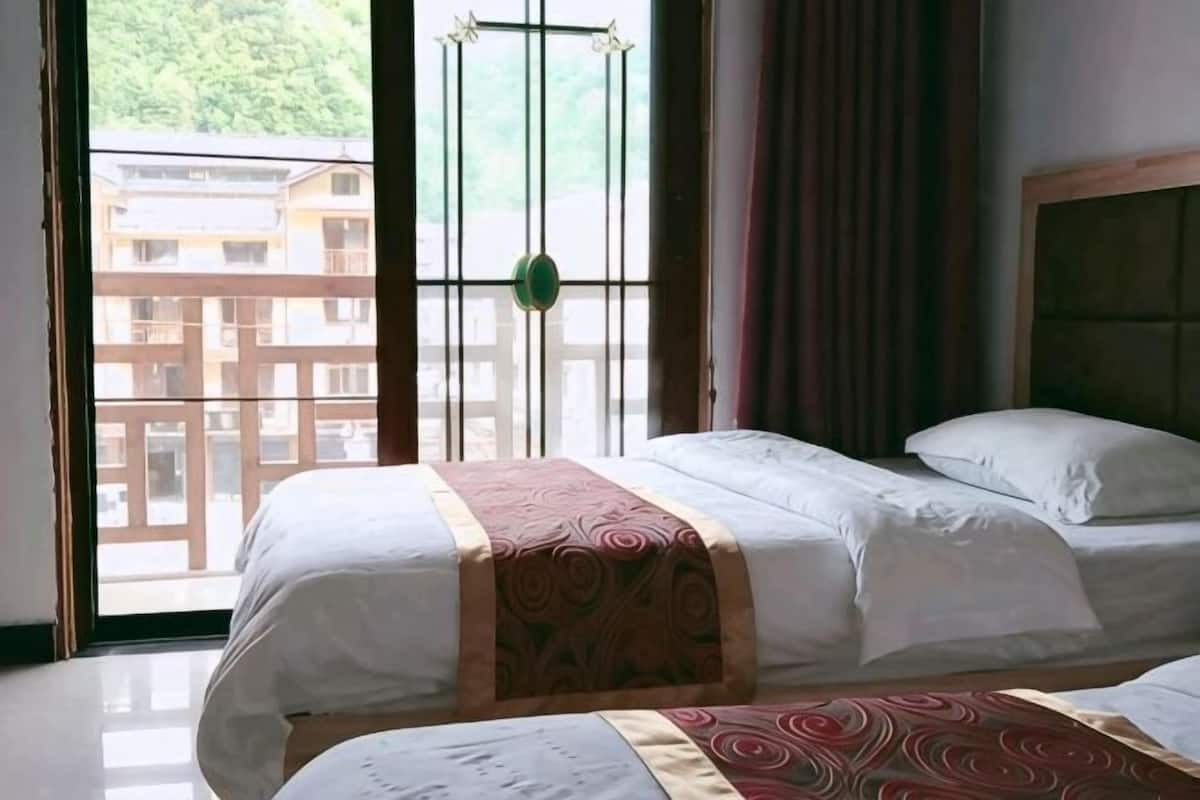 Ein Zimmer mit zwei Betten, einem Fenster mit Blick auf Gebäude und einem Vorhang.