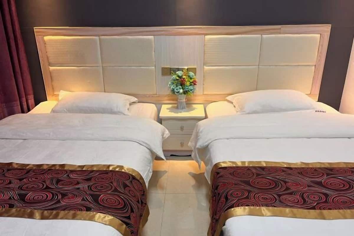 Ein Hotelzimmer mit zwei Betten, einem Nachttisch mit Blumenvase und einem hölzernen Kopfteil.