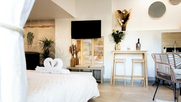 A modern hotel room with a large bed, a TV, a small desk with a chair, and a bathroom with a mirror and towel rack. - Suite soledad (Maraussan)