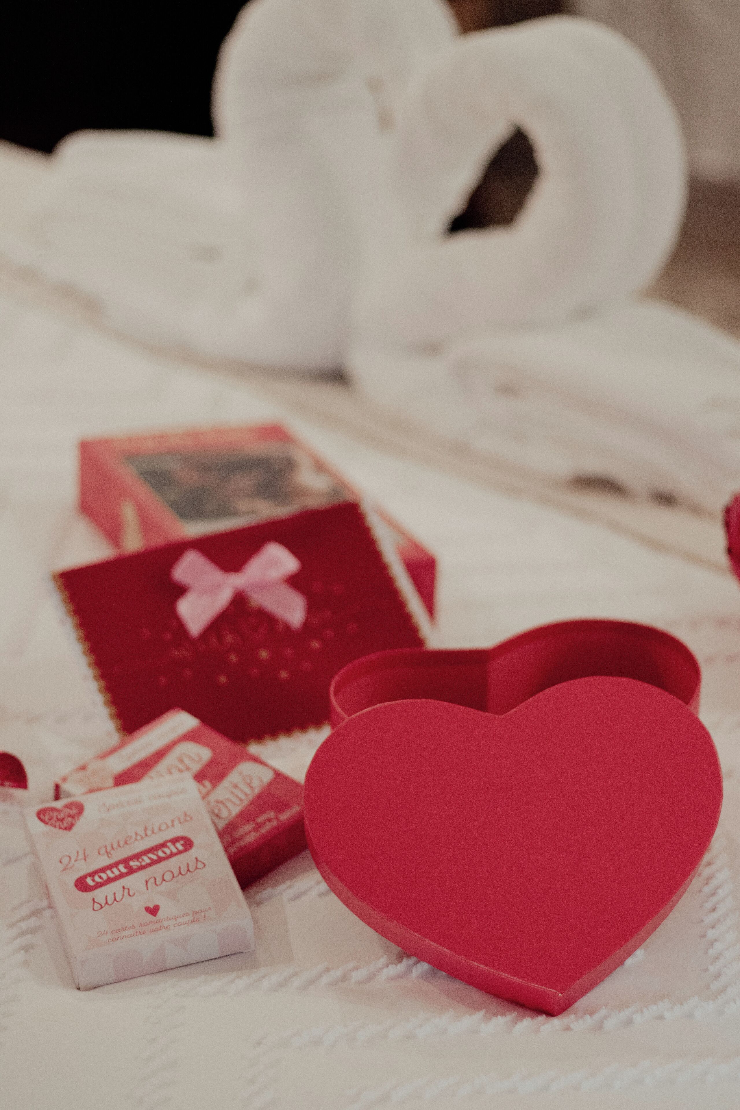 A bed with neatly arranged red and white items, including heart-shaped boxes and a book titled "24 questions tout savoir".
