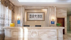 A reception desk with a framed sign, marble walls, and a potted plant. - Houten Hotel (Shantou)