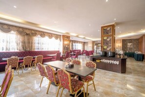 A hotel dining area with a long table, red upholstered seating, and a buffet station. - Houten Hotel (Shantou)