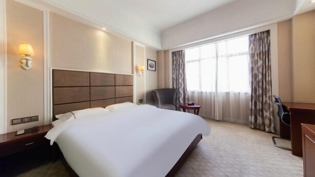 Een hotelkamer met een groot bed, een bureau, een stoel en een raam met gordijnen.