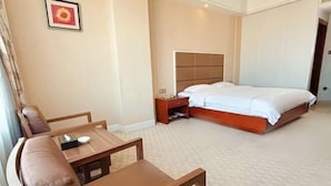 A hotel room with a bed, a wooden nightstand, a bedside table, a brown leather sofa, and a small wooden table. - Houten Hotel (Shantou)