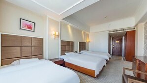 Een hotelkamer met drie bedden, een houten hoofdbord, een grote spiegel en een foto in een lijst aan de muur.