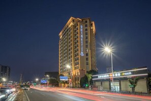 A multi-story hotel with a prominent vertical sign, a well-lit facade, and a busy street with light trails indicating traffic. - Houten Hotel (Shantou)