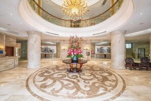 A grand lobby with marble floors, a central floral arrangement, and a chandelier. - Houten Hotel (Shantou)