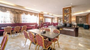 A spacious dining area with a long table and multiple chairs, a seating area with cushioned benches, and a buffet counter with various food items. - Houten Hotel (Shantou)
