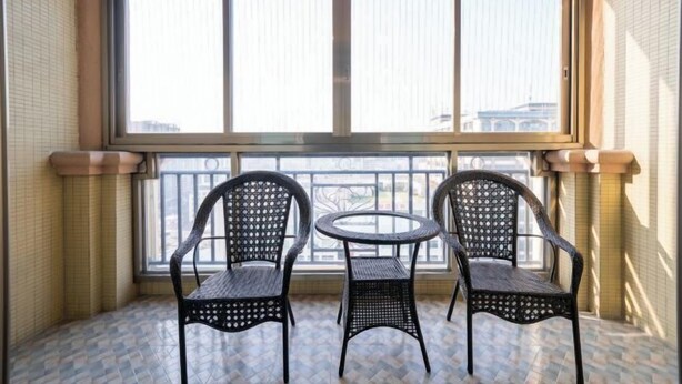 A balcony with two wicker chairs and a small round table, large windows, and tiled flooring. - Houten Hotel (Shantou)