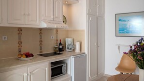 A kitchen with white cabinets, a coffee maker, a wine bottle, and a dish rack with fruits. - Marias Hospitality.Pure Paroshospitality (ΠΑΡΟΣ)
