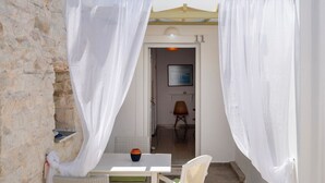 A small outdoor seating area with a table and chairs, a white umbrella, and a stone wall. - Marias Hospitality.Pure Paroshospitality (ΠΑΡΟΣ)