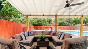 Eine Terrasse im Freien mit überdachter Sitzgruppe, Deckenventilator und Blick auf ein Schwimmbecken.