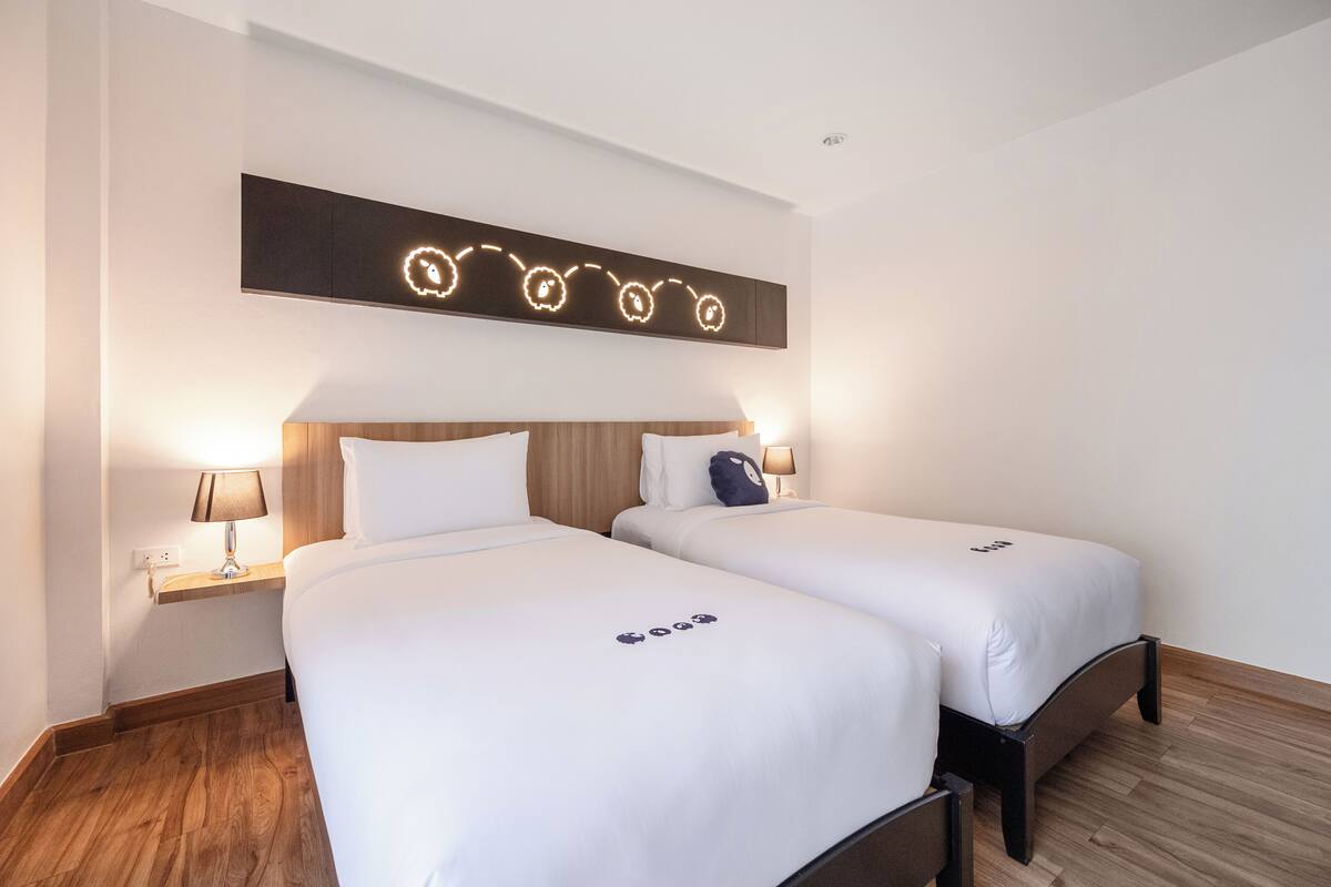 Habitación de hotel con dos camas, piso de madera y una lámpara fijada a la pared.