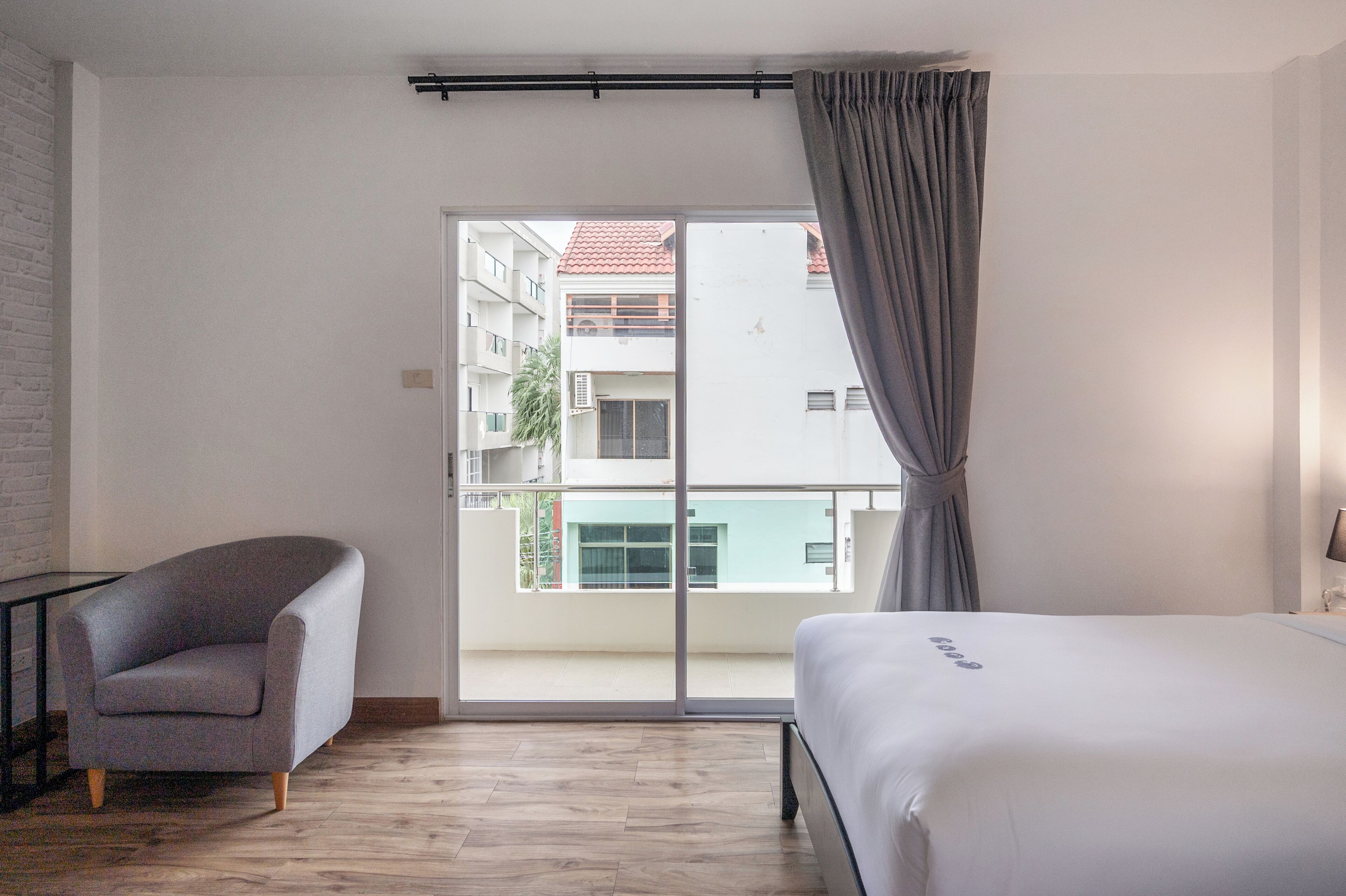 A hotel room with a bed, a chair, a window with curtains, and a view of buildings outside.
