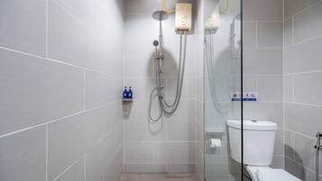 A modern bathroom with grey tiles, a glass shower enclosure, a white toilet, and a small shelf with toiletries.