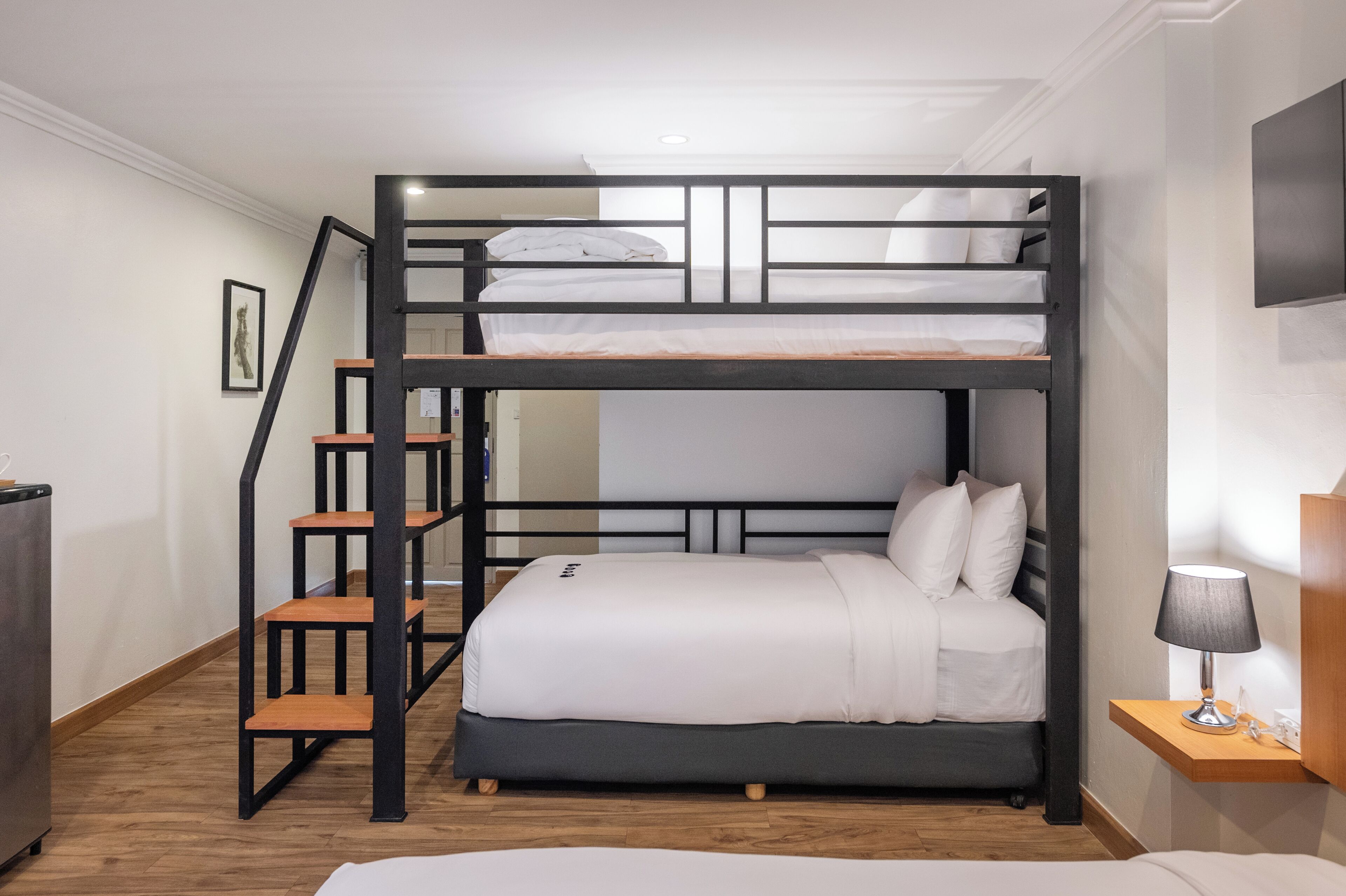 A bunk bed with a wooden ladder, a bedside table with a lamp, and a framed picture on the wall.