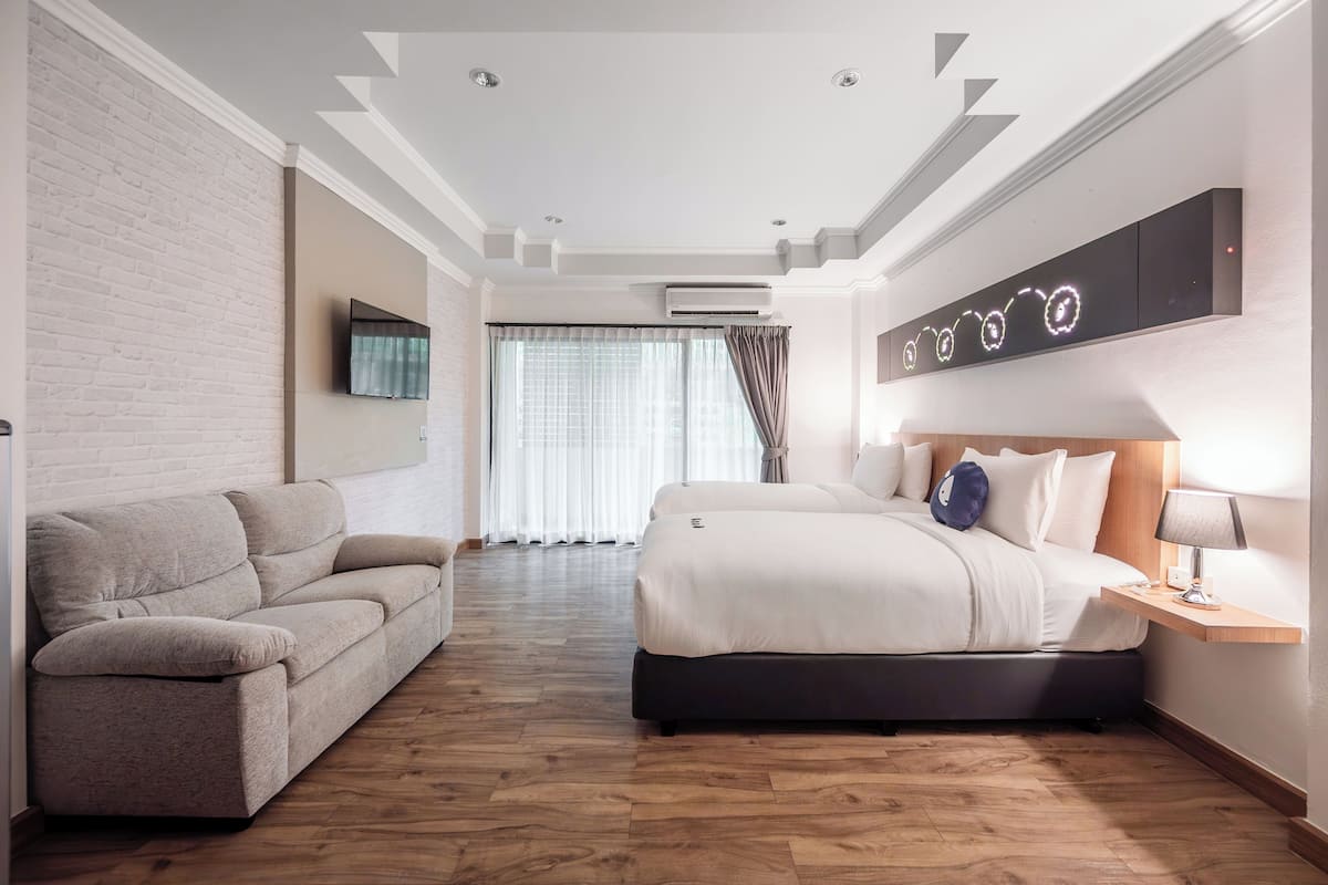 Habitación de hotel con cama, sofá, televisor de pantalla plana, aire acondicionado montado en la pared y ventana con cortinas.