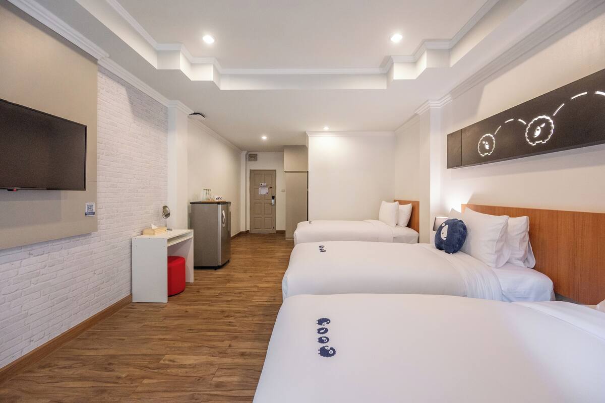 Habitación de hotel con dos camas, un televisor de pantalla plana montado en la pared, una pequeña kitchenette y piso de madera.