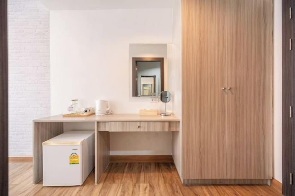 Una habitación compacta con escritorio de madera, refrigerador pequeño, espejo y armario.