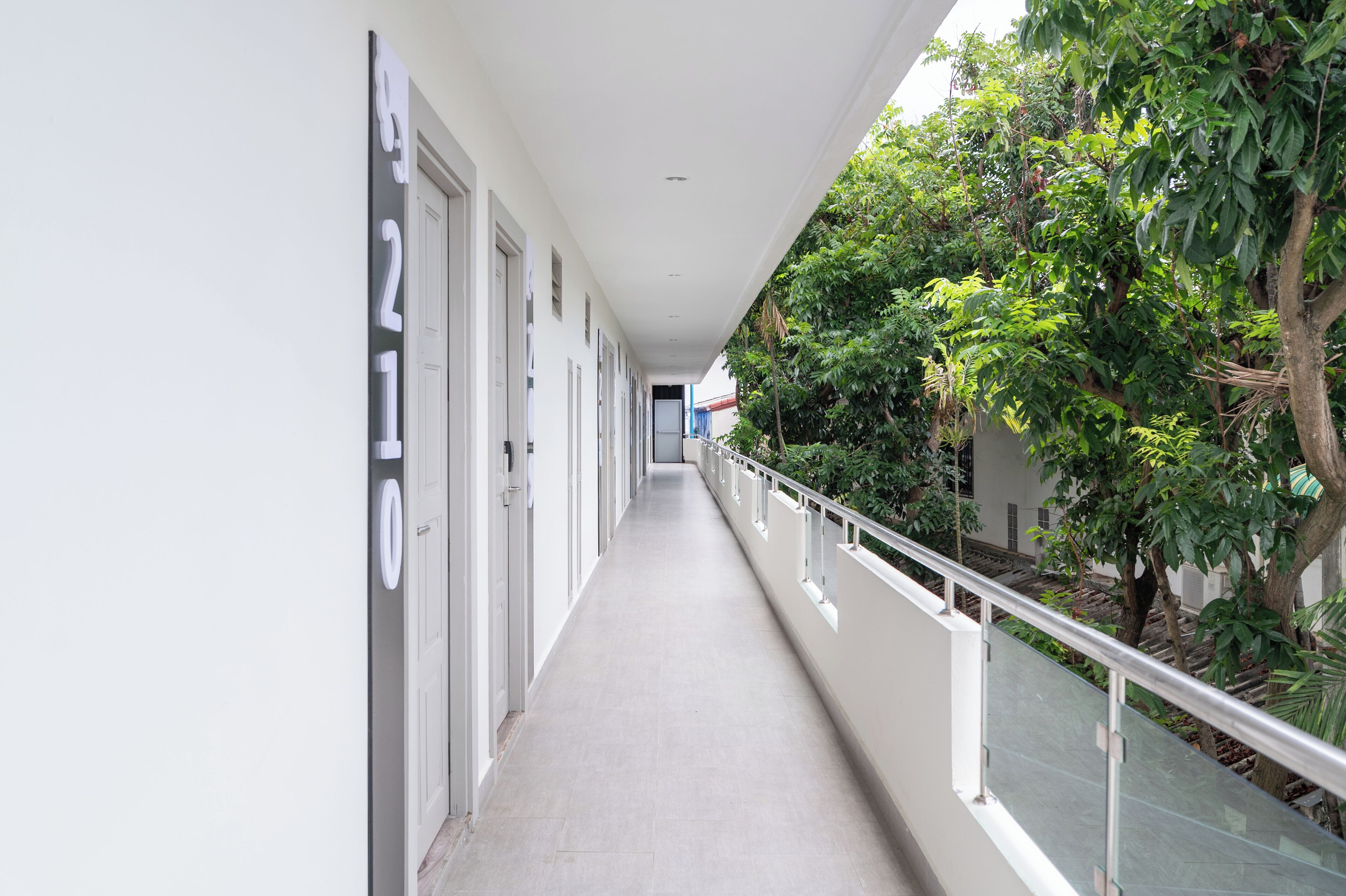 A corridor with doors numbered 9210, a glass railing, and greenery on one side.