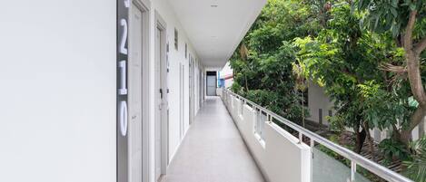A corridor with doors numbered 9210, a glass railing, and greenery on one side.