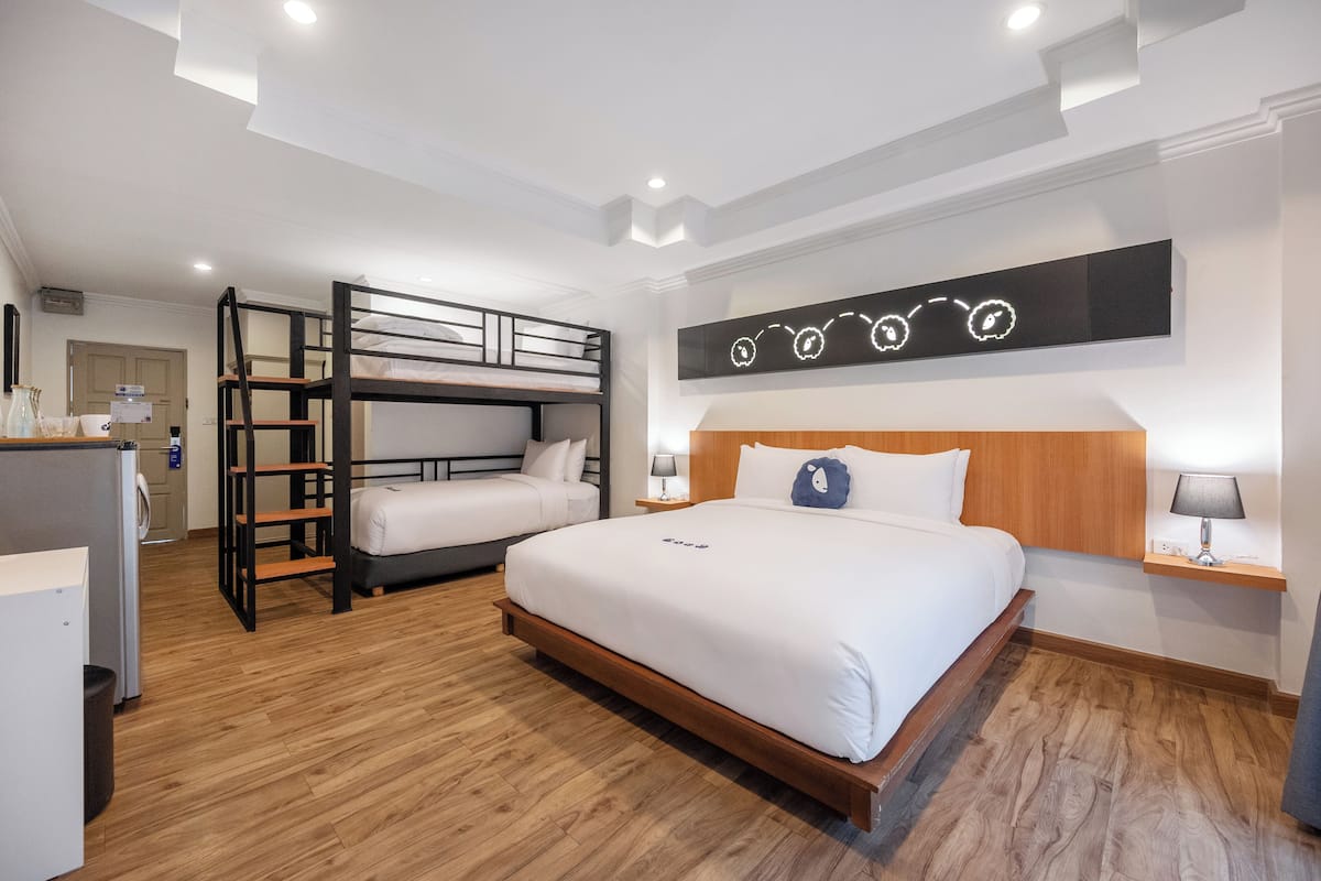 Una habitación de hotel con una cama litera, una cama individual, suelo de madera, un televisor montado en la pared y una mesita de noche con lámpara.