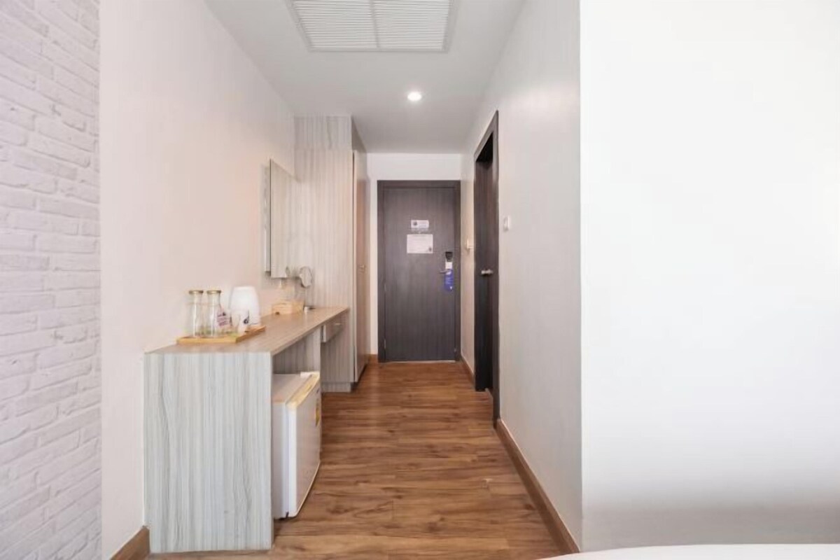 Un pasillo estrecho con suelo de madera, una pared de ladrillo blanco en un lado y una puerta al final.