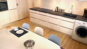 A compact kitchen with a black countertop, white cabinets, a built-in washing machine, and a dining area with a table and chairs.