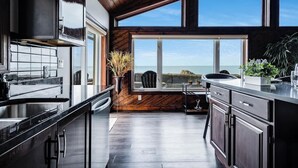 A modern kitchen with wooden accents, large windows, and a view of the sea.